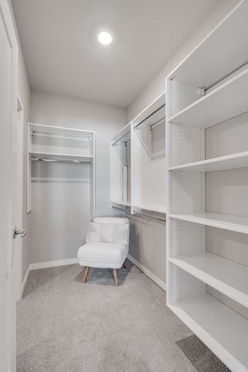 a walk in closet with white shelving and a white chair